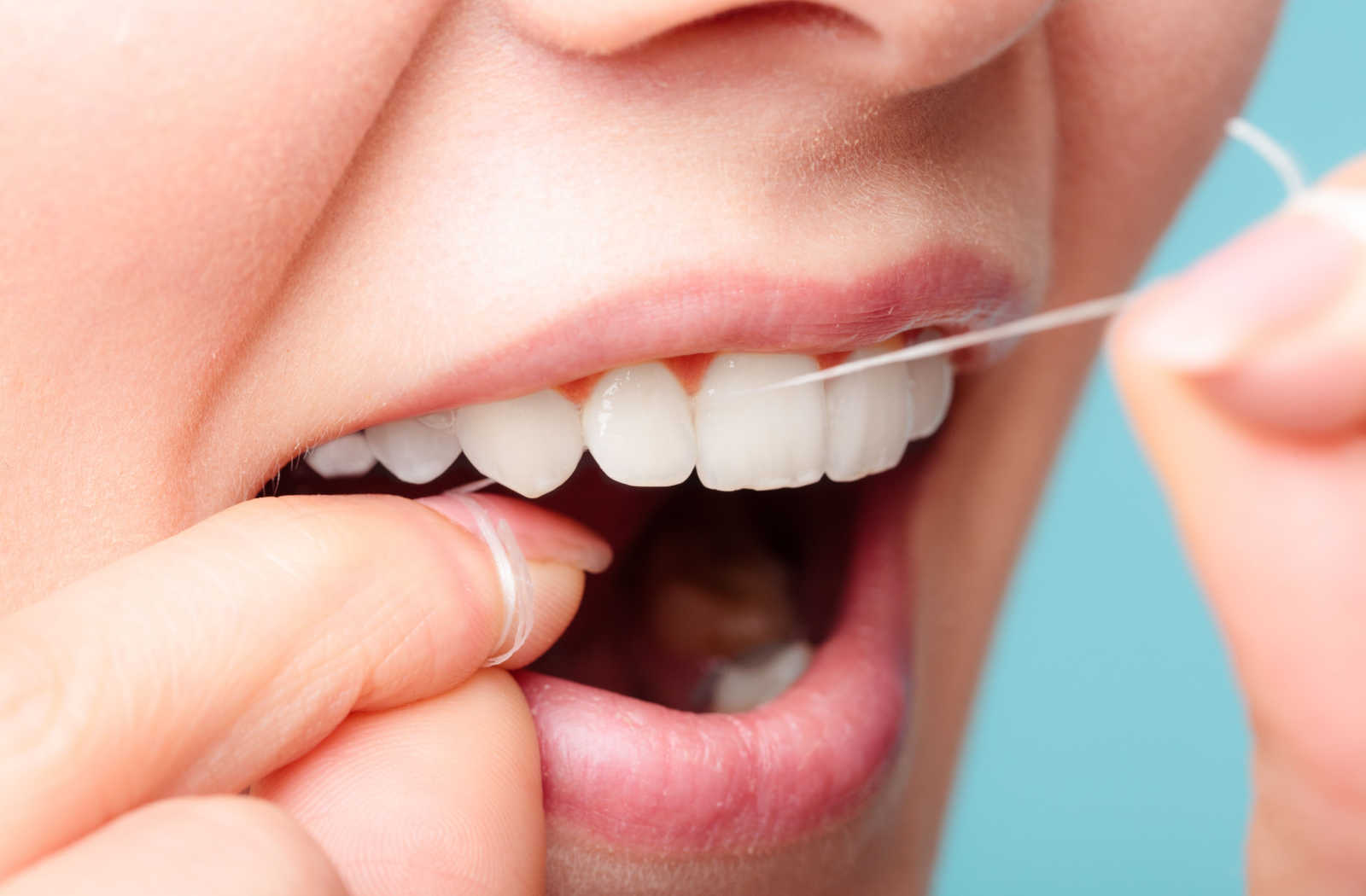 Close up image of a woman flossing her front upper teeth.