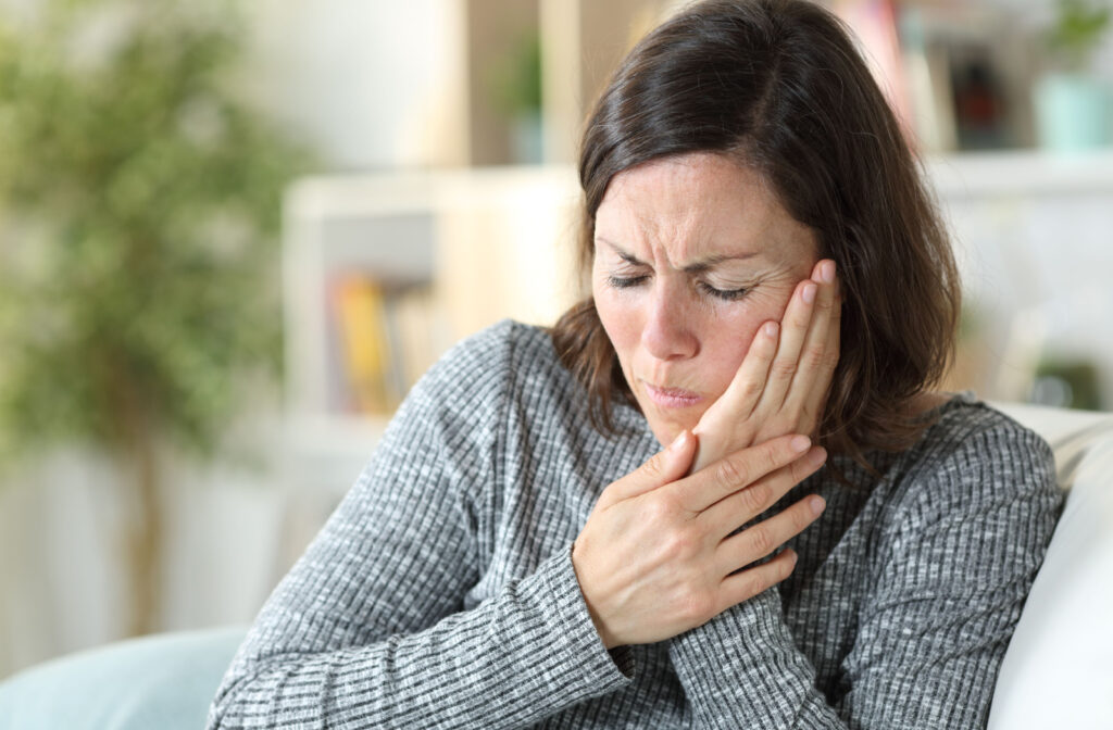 A woman experiencing gum discomfort holds her left cheek with her left hand.