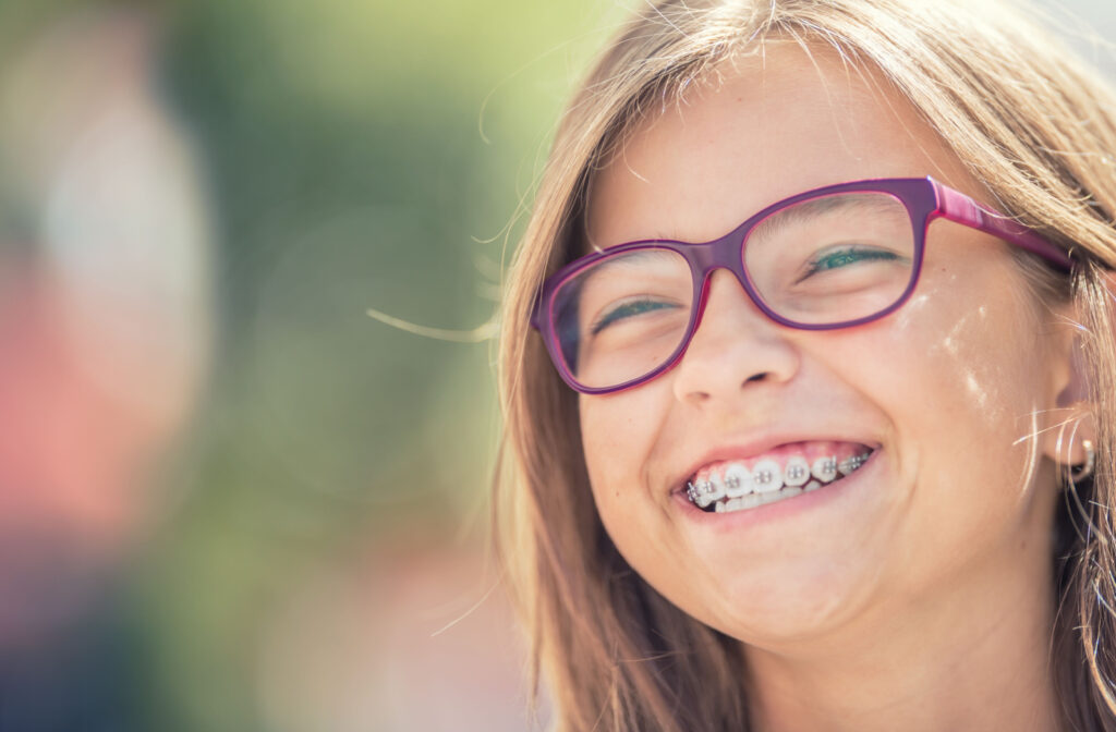 Close-up of a young child, smiling with dental braces and glasses.