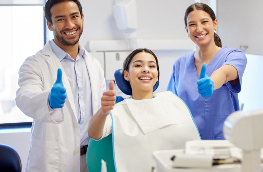 A patient in the exam chair smiles with their dental team, including their dentist and hygienist after a successful dental recall exam.