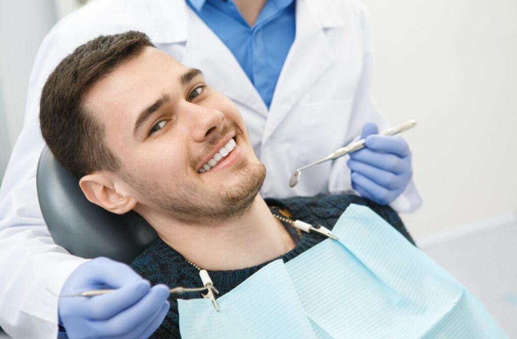 A close-up image of a smiling patient lying back in a dental chair and a dentist behind them during a routine exam.