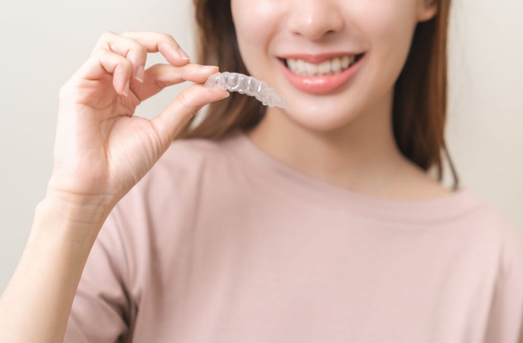 A woman holding up her invisalign aligners and smiling.