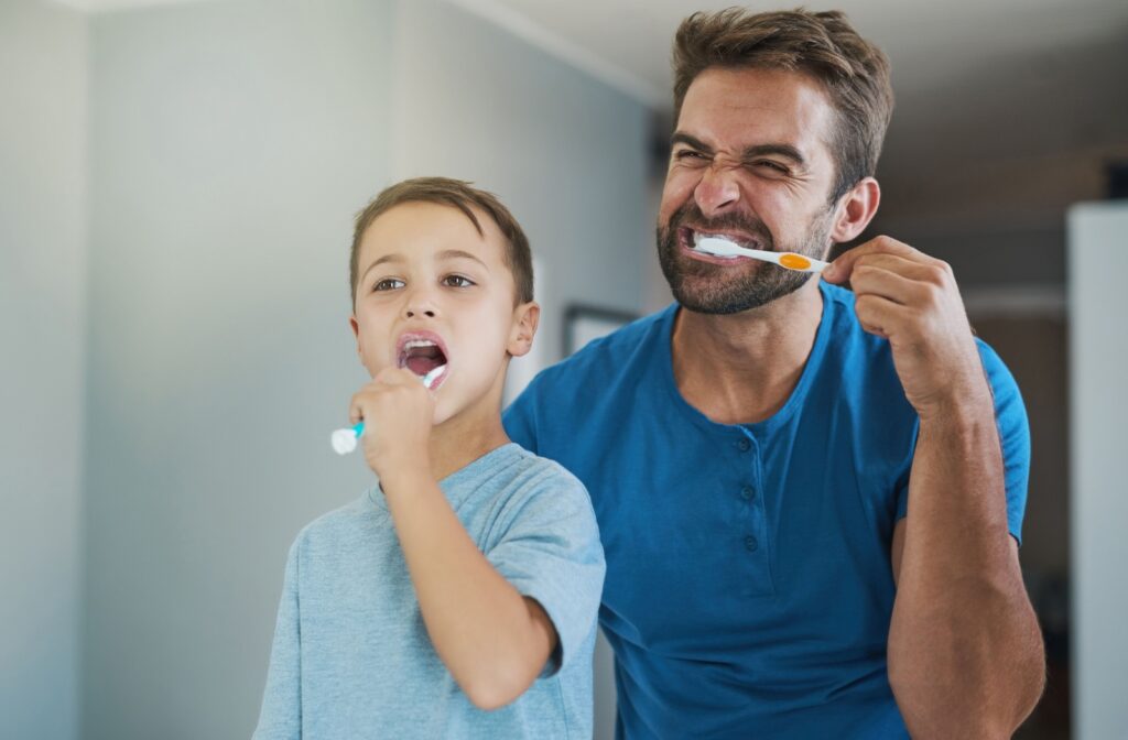 A parent and their young child brush their teeth together.