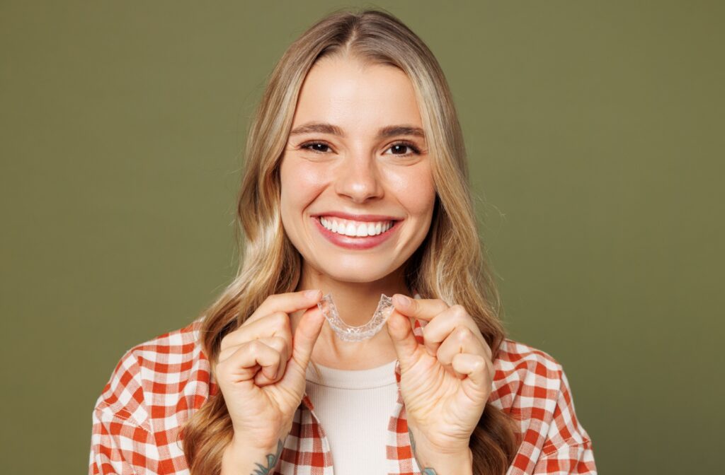 Young smiling woman holding up an Invisalign aligner with both hands.