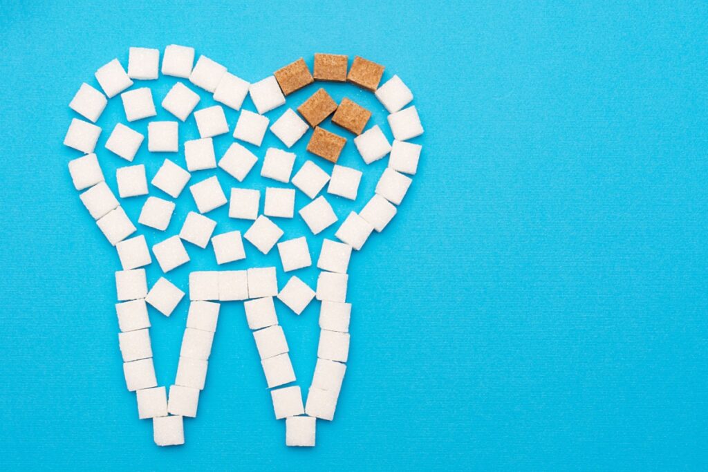 A tooth shape created from sugar cubes with a section showing enamel damage on a blue background.