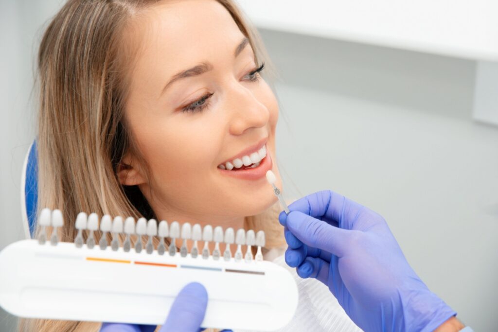 Smiling woman at dental appointment with dentist using tooth shade guide to match color for cosmetic dental treatment.